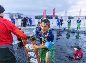 A wet 澳博体育app下载 employee wearing floaties, a rainbow lei, and plastic grass skirt climbs a ladder to exit the chilly lake waters as lifeguards dressed in cold water gear keep watch.