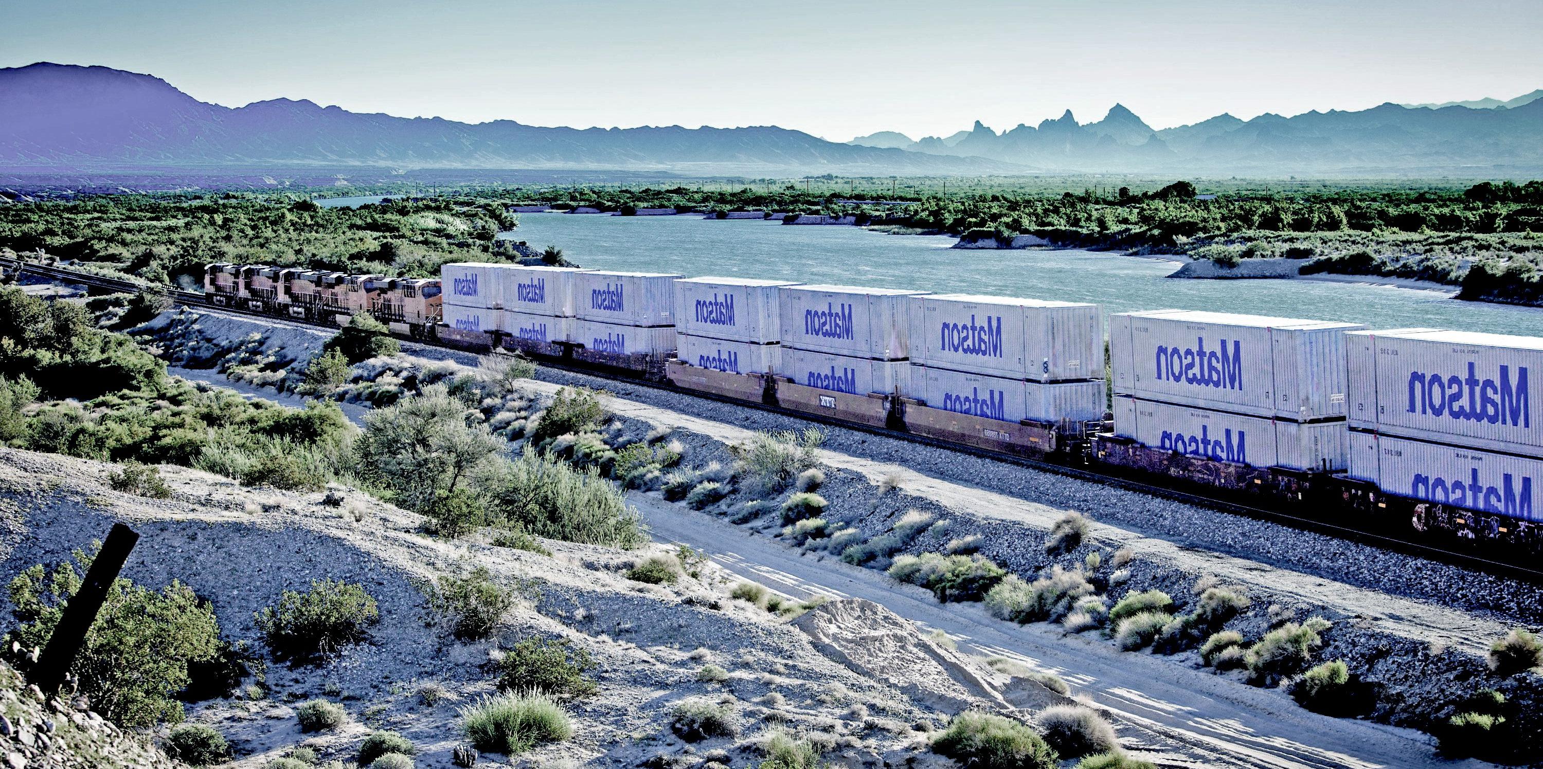 澳博体育app下载 Logistics' 53-foot intermodal containers on the rail with a river and mountains in the background.