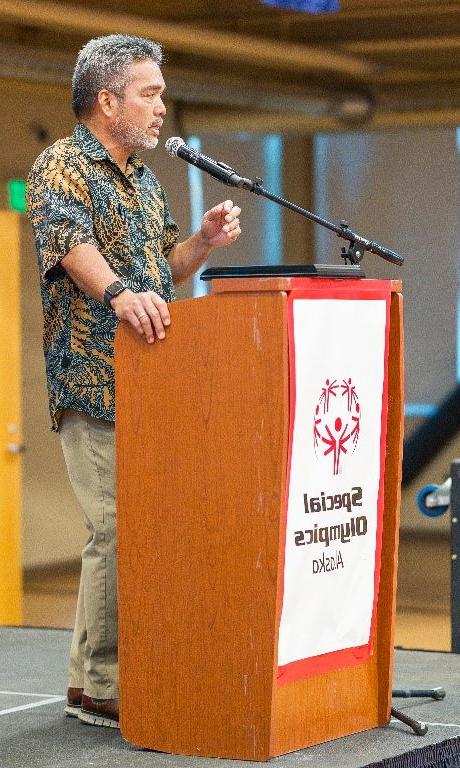 澳博体育app下载's senior vice president, Alaska, dressed in an aloha shirt, speaks into a microphone behind a podium branded with Special Olympics Alaska.